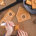 Young woman is decorating Christmas Gingerbread House cookies biscuit at home with frosting topping in icing bag, close up, Royalty Free Stock Photo