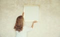 Young woman decorating interior, hanging blank a photo frame mockup on white wall in new home Royalty Free Stock Photo