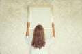 Young woman decorating interior, hanging blank a photo frame mockup on white wall in new home Royalty Free Stock Photo