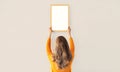 Young woman decorating interior, hanging blank a photo frame mockup on white wall in a new house Royalty Free Stock Photo