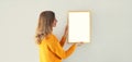 Young woman decorating interior, hanging blank a photo frame mockup on white wall in a new house Royalty Free Stock Photo