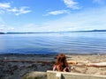 A young woman deep in thought sitting on a bench that looks outward to the ocean full of boats  on a beautiful sunny summer day Royalty Free Stock Photo