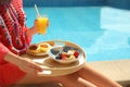 Young woman with delicious breakfast on tray near swimming pool, closeup. Space for text Royalty Free Stock Photo