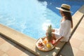 Young woman with delicious breakfast on tray near swimming pool. Space for text Royalty Free Stock Photo