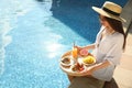 Young woman with delicious breakfast on tray near swimming pool. Space for text Royalty Free Stock Photo