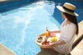 Young woman with delicious breakfast on tray near swimming pool. Space for text Royalty Free Stock Photo