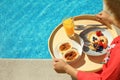 Young woman with delicious breakfast on tray near swimming pool, closeup. Space for text Royalty Free Stock Photo