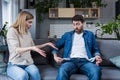 A young woman demands money from her husband, the man does not show empty pockets. At home, sitting on the couch. Quarrels, Royalty Free Stock Photo