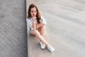 Young woman in denim shorts sitting on the waterfront. Beautiful girl posing on a background of the city on a sunny day. Girl in c Royalty Free Stock Photo