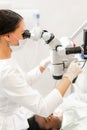 Young woman dentist treating root canals using microscope in the dental clinic. Man patient lying on dentist chair with Royalty Free Stock Photo