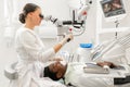 Young woman dentist treating root canals using microscope in the dental clinic. Man patient lying on dentist chair with Royalty Free Stock Photo