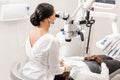 Young woman dentist treating root canals using microscope in the dental clinic. Man patient lying on dentist chair with Royalty Free Stock Photo