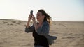 Young woman in desert taking photos on mobile phone. Sand storm, strong wind. Royalty Free Stock Photo