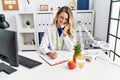 Young woman dietician talking on telephone writing on document at clinic Royalty Free Stock Photo