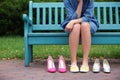 Young woman with different pairs of shoes sitting on bench outdoors