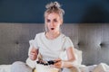 Young woman in disbelief watching TV while eating cake and holding a remote control while watching TV in bed. Surprised Royalty Free Stock Photo