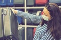 A young woman in a disposable mask choosing a suitcase for the upcoming vacation after the end of the Covid-19 coronavirus