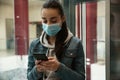 Woman with disposable mask and smartphone in elevator. Dangerous virus