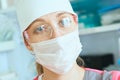 Young woman doctor anesthesiologist dressed in mask, glasses and hat ready for surgery and looking into the camera