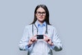 Young woman doctor holding credit card on light gray background Royalty Free Stock Photo