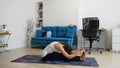 Young woman does yoga at home bending knees to her chest in pindasana pose