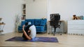 Young woman does yoga at home bending knees to her chest in pindasana pose