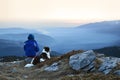 Young woman and dog admiring sunrise high in the mountain