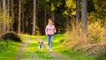 Young woman and dog running together on country in forest. Cheerful female exercising outdoor with her pet Royalty Free Stock Photo