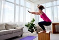 Young woman doing box jump exercise in living room at home, copy space. Jumping squats, side view. Royalty Free Stock Photo