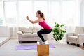 Young woman doing box jump exercise in living room at home, copy space. Jumping squats. Sport, healthy lifestyle concept. Royalty Free Stock Photo