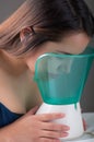 Young woman doing inhalation with a medical vaporizer nebulizer machine on black background