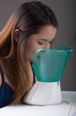 Young woman doing inhalation with a medical vaporizer nebulizer machine on grey background