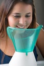 Young woman doing inhalation with a medical vaporizer nebulizer machine on grey background