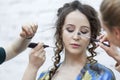 A young woman is doing make-up. Bright brunette with curly hair. Beauty industry. Close-up. Light background