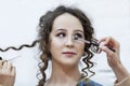 A young woman is doing make-up. Bright brunette with curly hair. Beauty industry. Close-up. Light background