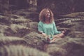 Young woman doing meditation by sitting in forest with eyes closed. Caucasian woman doing yoga for fitness at park. Carefree woman