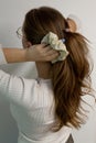 Young woman doing a ponytail with beige hair tie, scrunchie, view from the back against white background Royalty Free Stock Photo