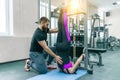 Young woman doing rehabilitation exercises with personal instructor using kinesi machine, fitness gym background. Kinesis