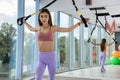 Young woman doing workout with trx straps training arms in fitness gym