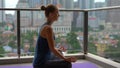 Young woman doing yoga exercises on her balcony in multi-storey building with a view on a downtown with skycrappers