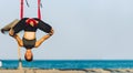 Young woman doing yoga exercises with swing upside down on the beach in front of the sea