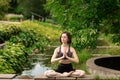 Young woman doing yoga. Girl sitting in the lotus position in the park near a small decorative lake Royalty Free Stock Photo