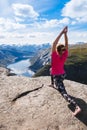 Young woman doing yoga on Trolltunga. Happy girl enjoy beautiful lake and good weather in Norway. Royalty Free Stock Photo