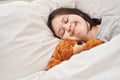 Young woman with down syndrome lying on bed sleeping with teddy bear at bedroom