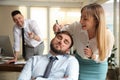 Young woman drawing on colleague`s face while he sleeping in office. Funny joke Royalty Free Stock Photo