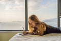 Young woman draws on a tablet against the background of a window with a sea view. Designer, sketching Royalty Free Stock Photo