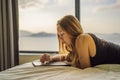Young woman draws on a tablet against the background of a window with a sea view. Designer, sketching Royalty Free Stock Photo