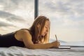 Young woman draws on a tablet against the background of a window with a sea view. Designer, sketching Royalty Free Stock Photo