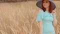 Young woman in dress and hat standing in wheat field. Pretty lady poses, standing in ears of wheat. Royalty Free Stock Photo