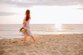 Young woman in a dress holding straw hat and walking alone on empty sand beach at sunset sea shoreand smiling. Single or divorsed Royalty Free Stock Photo